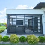 Przesuwna zabudowa tarasu z aluminium . Nowoczesny balkon z osłonami z drewna i metalowych lameli na domu jednorodzinnym.