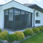 Przesuwna zabudowa tarasu z aluminium . Nowoczesna zadaszona weranda z żaluzjami na domu jednorodzinnym.