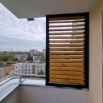 Zabudowa balkonu rama i lamele drewniane. Nowoczesny balkon z drewnianą osłoną i widokiem na miasto.