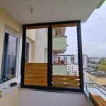 Zabudowa balkonu rama i lamele drewniane. Nowoczesny balkon z drewnianymi elementami i osłonami, widok na miasto.