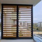 Zabudowa balkonu rama i lamele drewniane. Nowoczesny balkon z drewnianymi żaluzjami i widokiem na miasto.