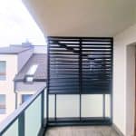 Zabudowa balkonu z aluminiowymi lamelami. Nowoczesny balkon z czarną osłoną z lameli na tle miejskiej architektury.