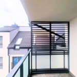 Zabudowa balkonu z aluminiowymi lamelami. Nowoczesny balkon z czarną metalową balustradą i osłoną na balkon w bloku mieszkalnym.