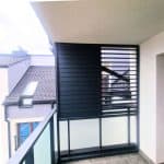 Zabudowa balkonu z aluminiowymi lamelami. Nowoczesny balkon z czarnymi żaluzjami i szklanymi panelami.