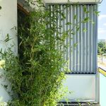 Zabudowa balkonu z lamelami pion aluminium. Zielona roślina na balkonie z metalową osłoną w tle.