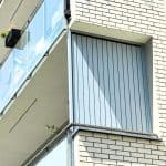 Nowoczesny balkon z szklanym balustradem i metalową osłoną na tle białej cegły.