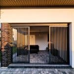 Zabudowa tarasu z lamelami aluminium pion. Nowoczesny garaż z metalowymi drzwiami przesuwanymi na podwórku.