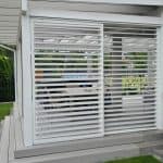 Przesuwna zabudowa tarasu z aluminium RAL 7047. Biała pergola z żaluzjami na tarasie, nowoczesny design, idealna do relaksu na świeżym powietrzu.