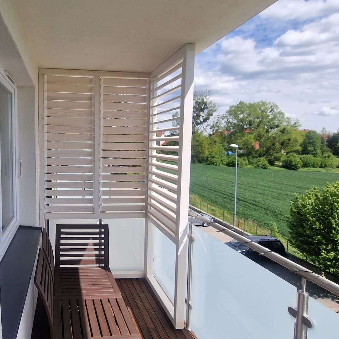 Zabudowa balkonu drewno białe poziom. Widok na balkon z drewnianymi meblami i zielonym krajobrazem w tle.