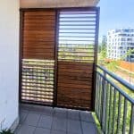 Nowoczesny balkon z drewnianą osłoną i widokiem na miasto.