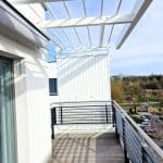 Zabudowa balkonu aluminiowa pion RAL 9016. Nowoczesny balkon z metalowym ogrodzeniem i drewnianą podłogą na świeżym powietrzu.
