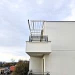 Zabudowa balkonu aluminiowa pion RAL 9016. Nowoczesny balkon na białym budynku z metalowymi barierkami i konstrukcją do suszenia.