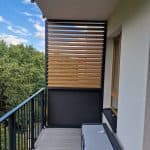 Nowoczesny balkon z drewnianymi panelami i widokiem na zieleń.