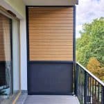 Balkon z drewnianą osłoną i widokiem na drzewa.