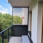 Nowoczesny balkon z drewnianymi lamelami i widokiem na zieleń.