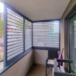 Boczna zabudowa balkonu aluminium RAL 7037. Nowoczesny balkon z roletami zewnętrznymi i meblami ogrodowymi.