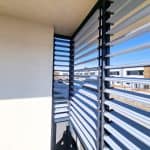 Zabudowa balkonu z aluminium RAL 7001. Nowoczesny balkon z żaluzjami aluminiowymi na tle nieba i miasta.