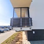 Zabudowa balkonu z aluminium RAL 7001. Nowoczesny balkon z metalowymi barierkami na białym budynku.