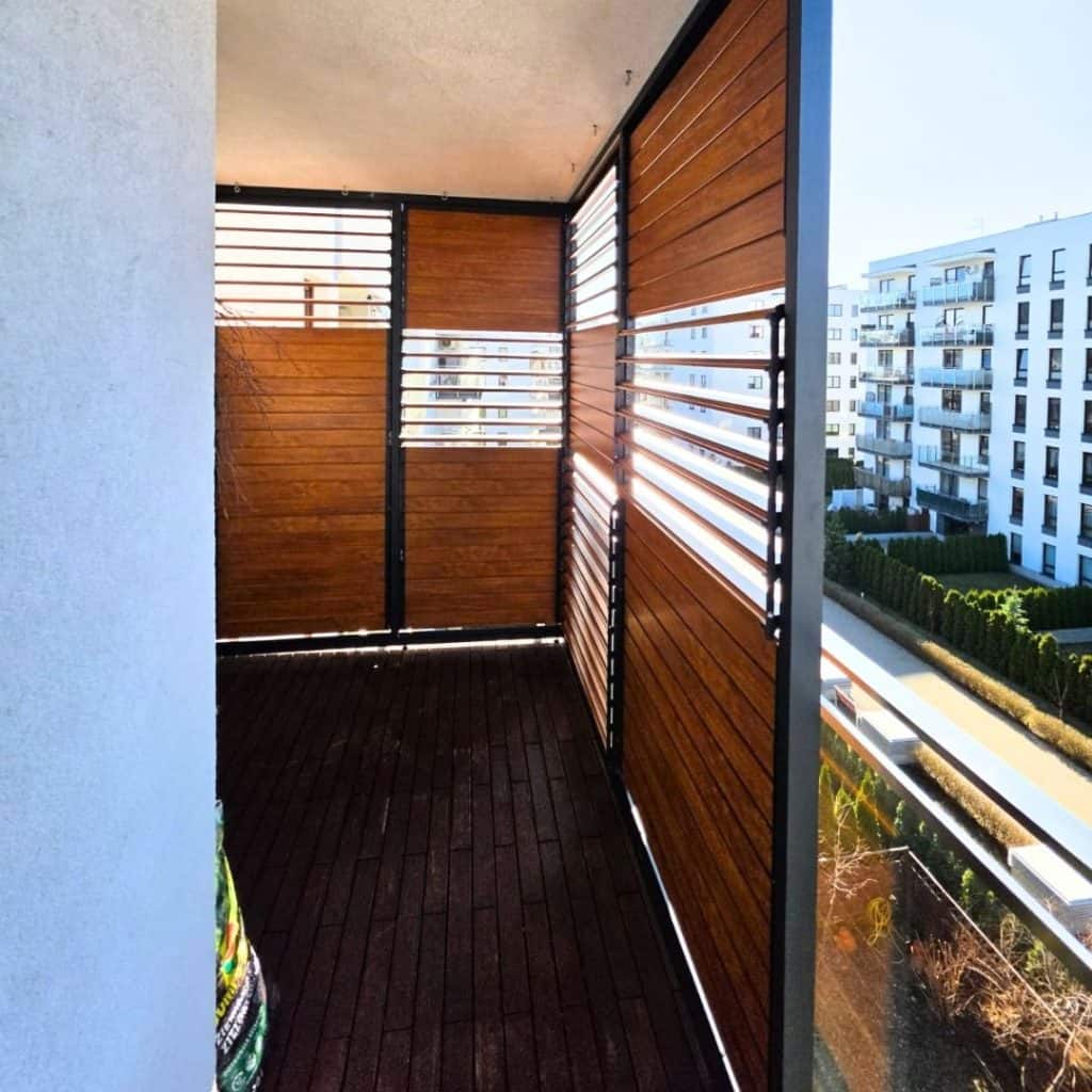 Nowoczesny balkon z drewnianymi osłonami i widokiem na miasto.